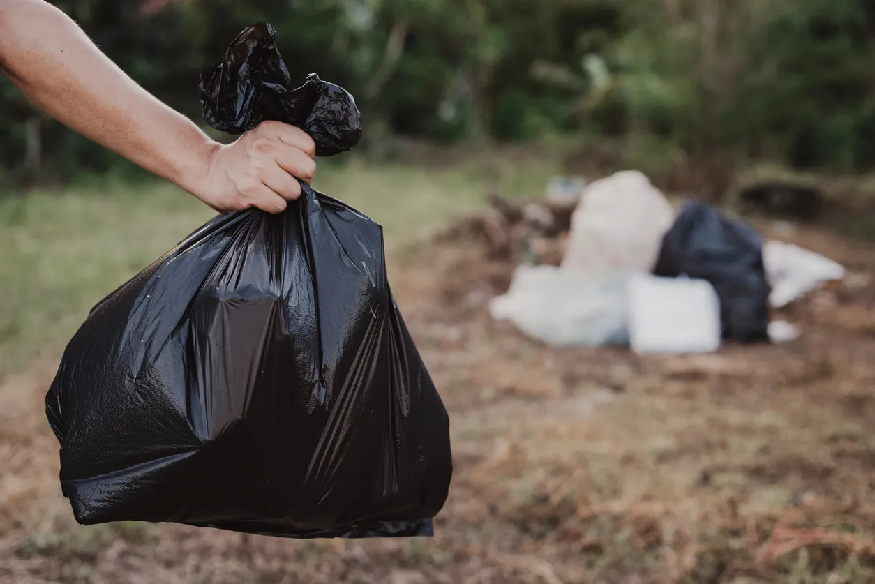 Photograph of a hand holding a trash bag with a blurred outdoor scene in the background